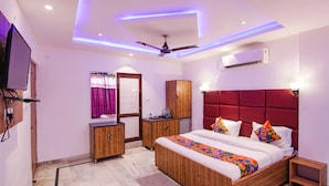 A bedroom with a bed, a ceiling fan, an air conditioning unit, wooden furniture, and a television. - Fabhotel Grover (Kangra)