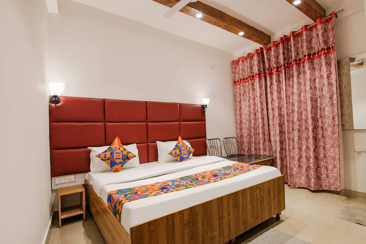 A bedroom with a wooden bed, red headboard, and patterned curtains.