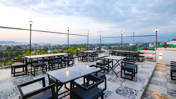 A rooftop terrace with tables and chairs, a view of the city, and street lamps. - Fabhotel Grover (Kangra)