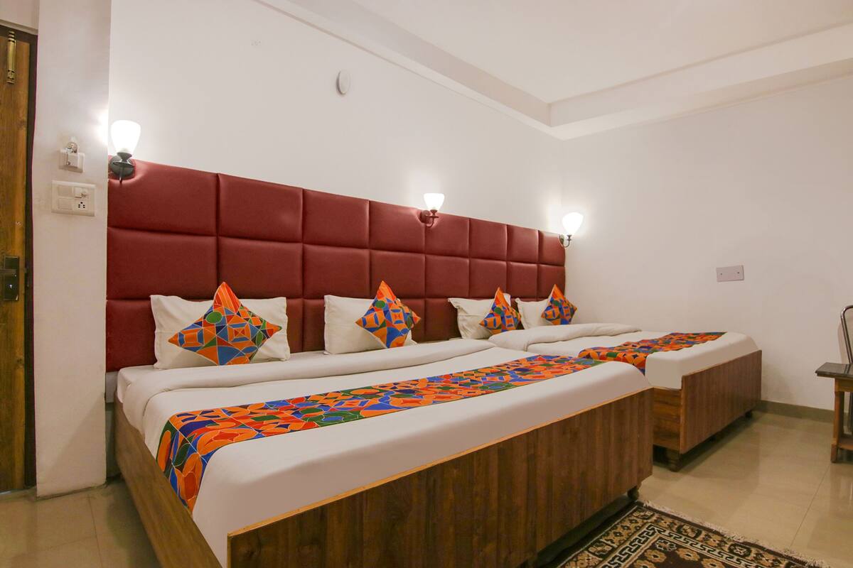 A hotel room with a large bed, two smaller beds, a red headboard, and a patterned bedspread.