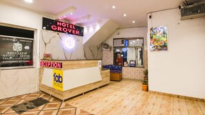 A hotel reception area with a reception desk, a neon sign, a wall-mounted fan, and a framed picture. - Fabhotel Grover (Kangra)