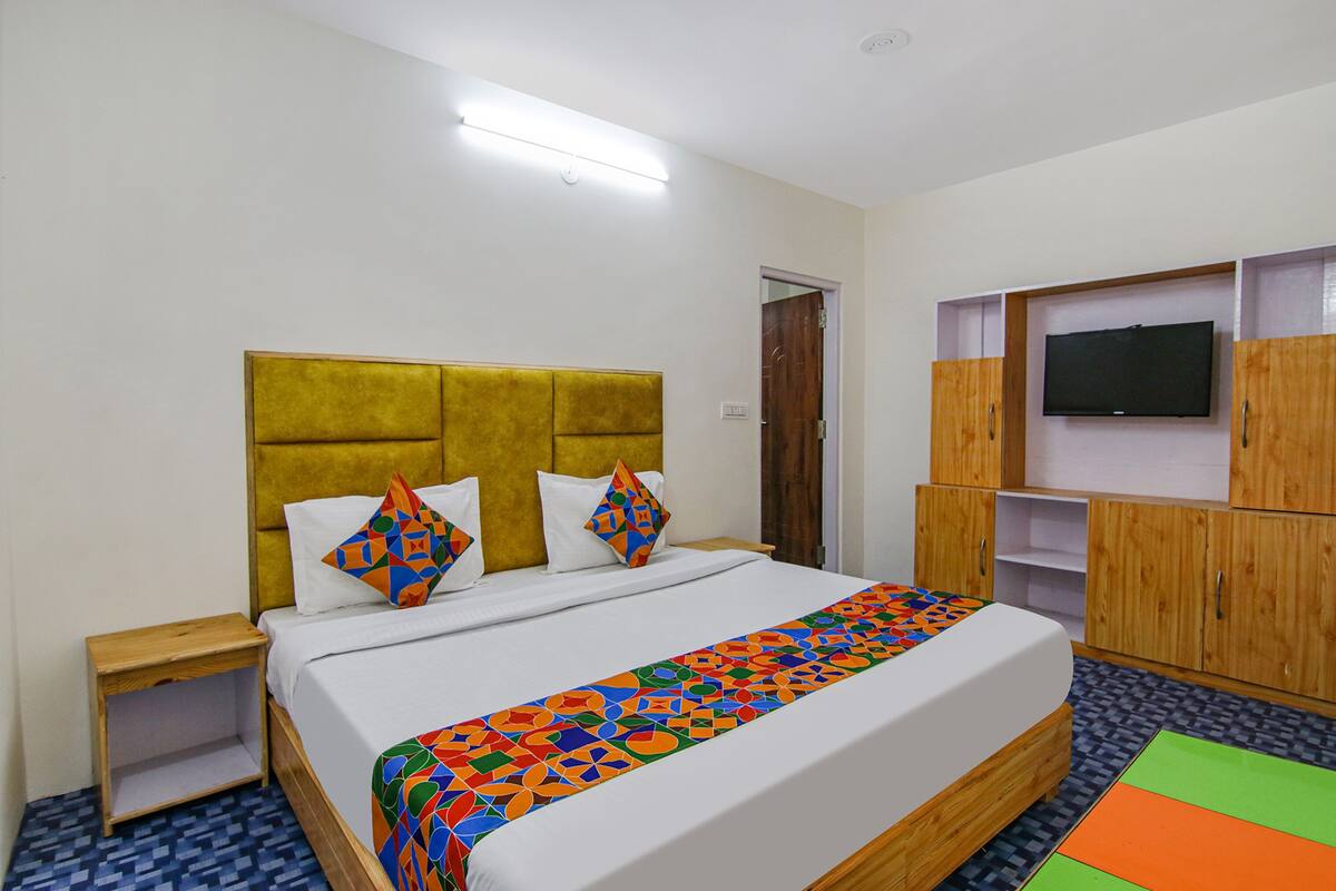 A hotel room with a bed, a TV mounted on the wall, and a wooden wardrobe.