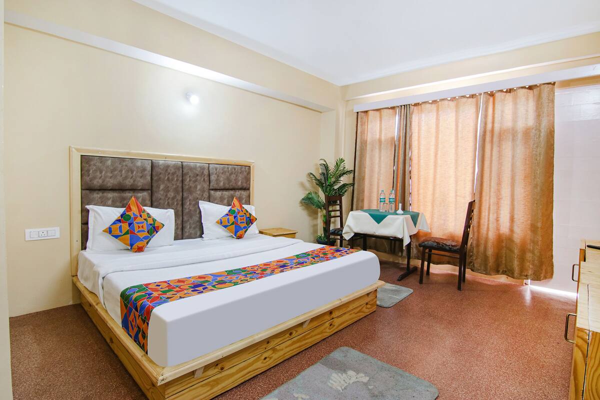 A hotel room with a large bed, a desk, a chair, a table, and a window with curtains.