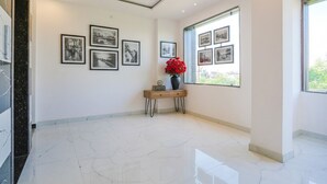 A spacious room with a marble floor, a wooden console table with a vase of red flowers, and framed pictures on the walls. - Fabhotel Relax Inn I (Kanpur)