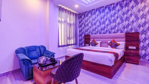 A modern bedroom with a large bed, a blue armchair, a wooden side table, and a black upholstered chair. - Fabhotel Relax Inn I (Kanpur)