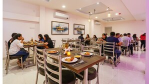 A dining area with multiple tables and chairs, people dining, and artwork on the walls. - Fabhotel Relax Inn I (Kanpur)