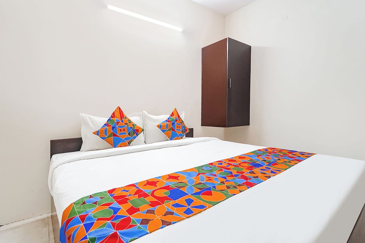 Habitación de hotel con cama, paredes blancas, armario marrón oscuro y almohadas y colcha con estampados geométricos coloridos.