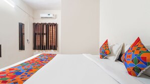 A hotel room with a bed, a window with curtains, an air conditioning unit, and a colorful runner on the bed. - Via Epic Residency (Chennai)
