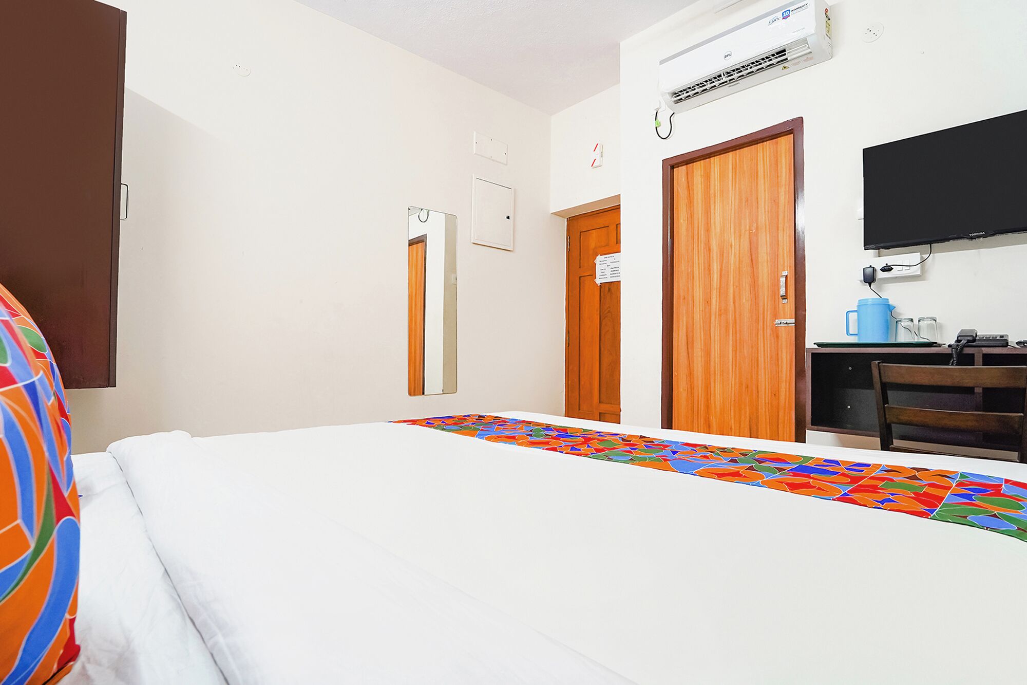 Habitación de hotel con cama, escritorio con computadora, televisor y aire acondicionado.