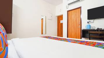 Habitación de hotel con cama, escritorio con computadora, televisor y aire acondicionado.
