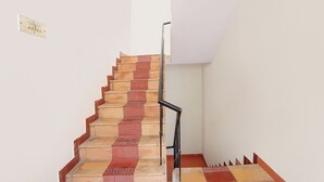 A staircase with alternating red and beige steps, a black handrail, and a white wall. - Via Epic Residency (Chennai)