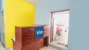A reception desk with a 'Via' sign, a door leading outside, and a red car parked outside. - Via Epic Residency (Chennai)