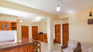 A spacious living area with a wooden dining table, a sofa, and a kitchen area with wooden cabinets and a countertop. - Fabhotel Orchard Retreat (Manali)