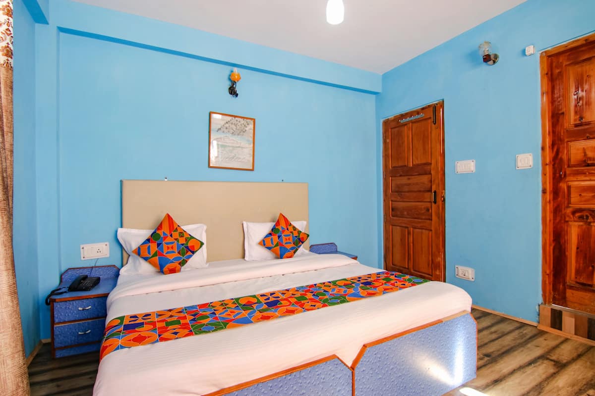 A bedroom with a bed, a nightstand, a wooden door, and a wall with a light switch.