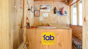 A wooden reception desk with a 'fab hotels' sign, framed pictures, and a fire extinguisher on the wall. - Fabhotel Orchard Retreat (Manali)