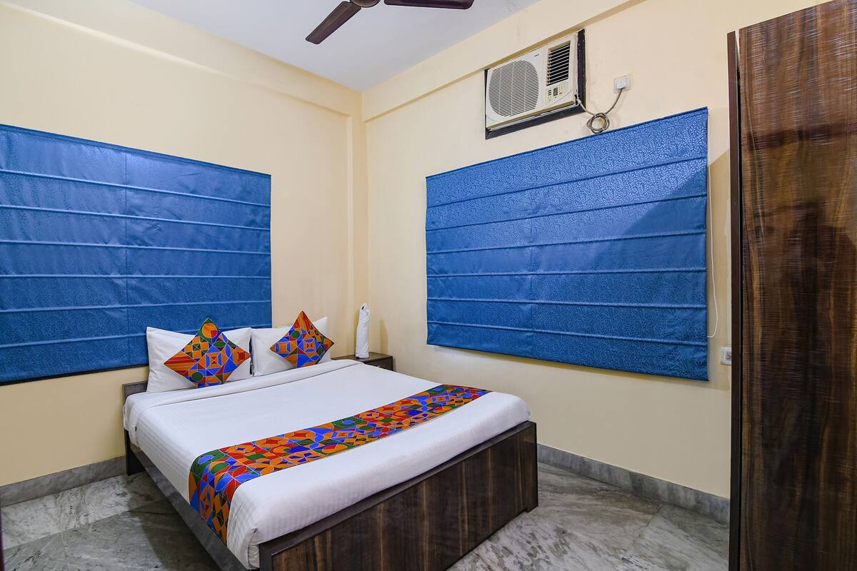 A hotel room with a bed, a ceiling fan, an air conditioning unit, and a wooden door.