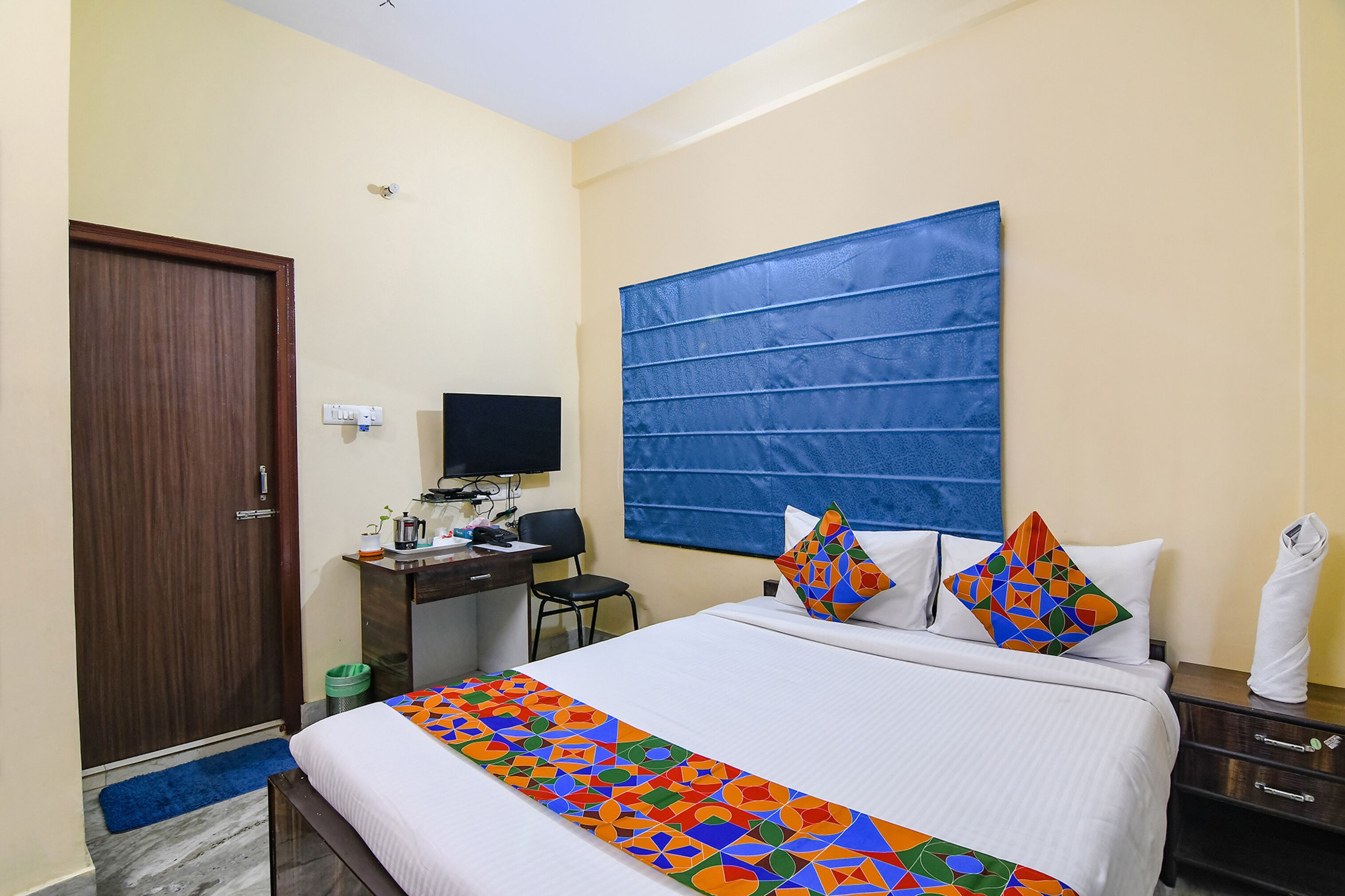 Une chambre d’hôtel avec un lit, un bureau équipé d’un ordinateur, une chaise et une tête de lit bleue.