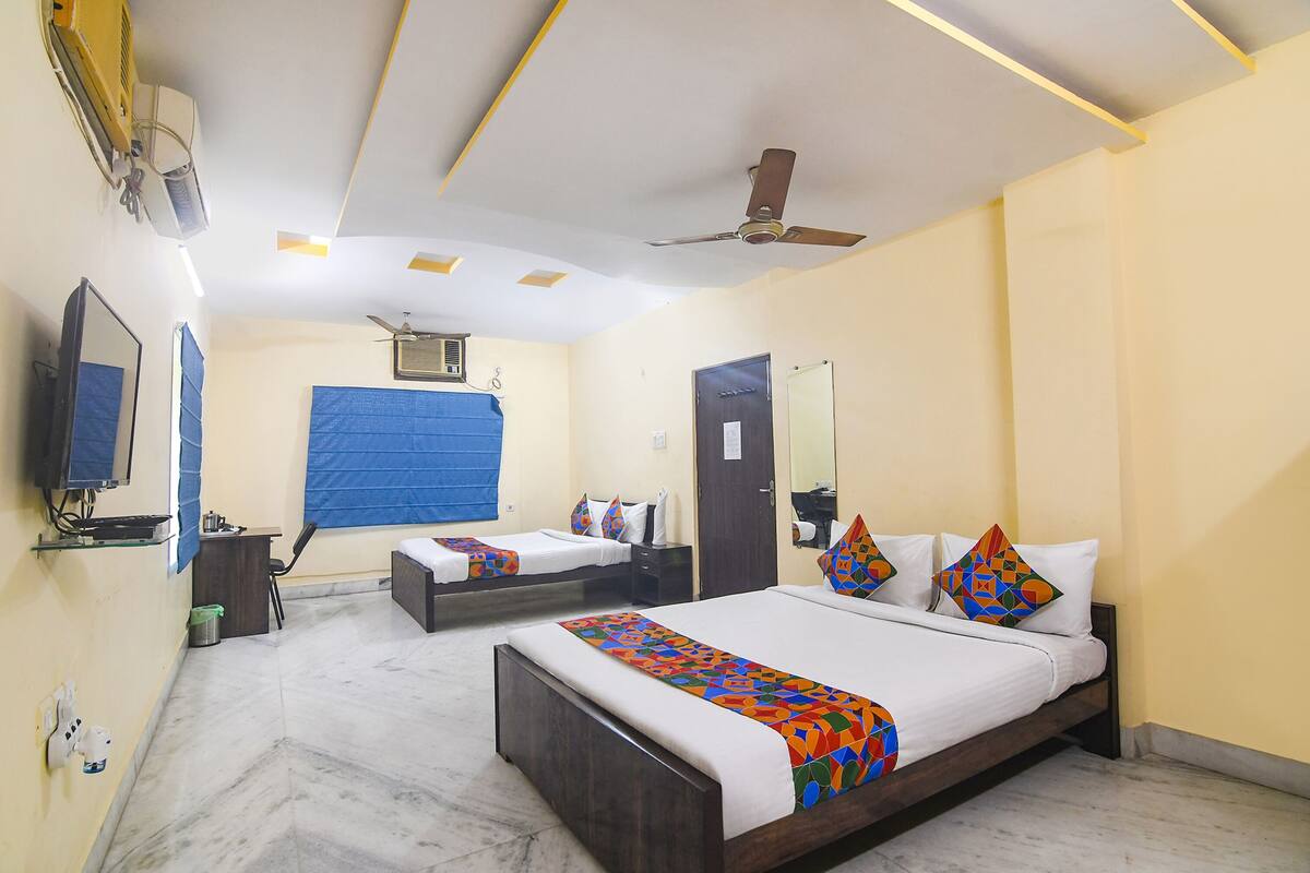 A hotel room with two single beds, a large bed, a ceiling fan, a TV, and a desk with a chair.