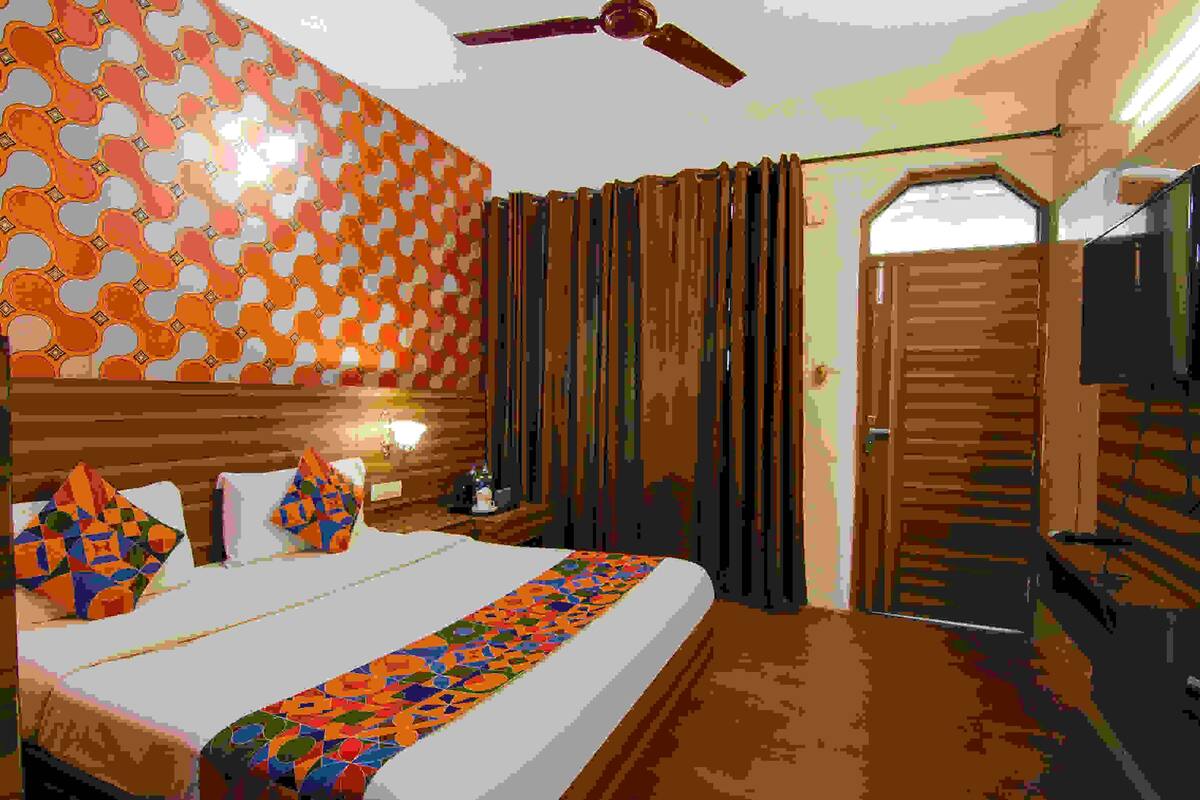 A hotel room with a bed, a nightstand, a ceiling fan, a TV, and a wooden door.