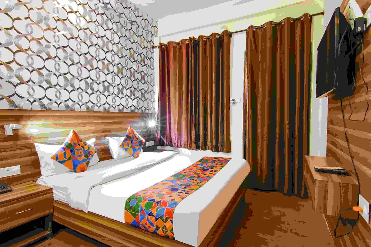 A hotel room with a bed, a nightstand, a wall with a circular pattern, and a curtain.