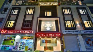 Un edificio con un cartello che riporta 'Hotel & Restro', 'D.K. Super Market' e 'Hitesh Glass' al piano terra.