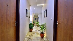 Corridoio di un albergo con porte in legno, quadri appesi e piante in vaso.
