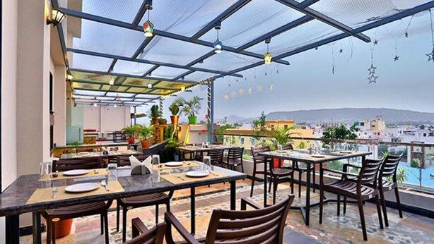 Zona pranzo all'aperto con tavoli e sedie, vista sulla città e soffitto con ventola e luci.