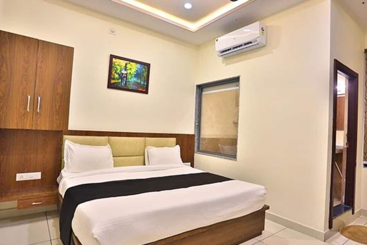 A hotel room with a bed, wooden wardrobe, air conditioning unit, and a window.