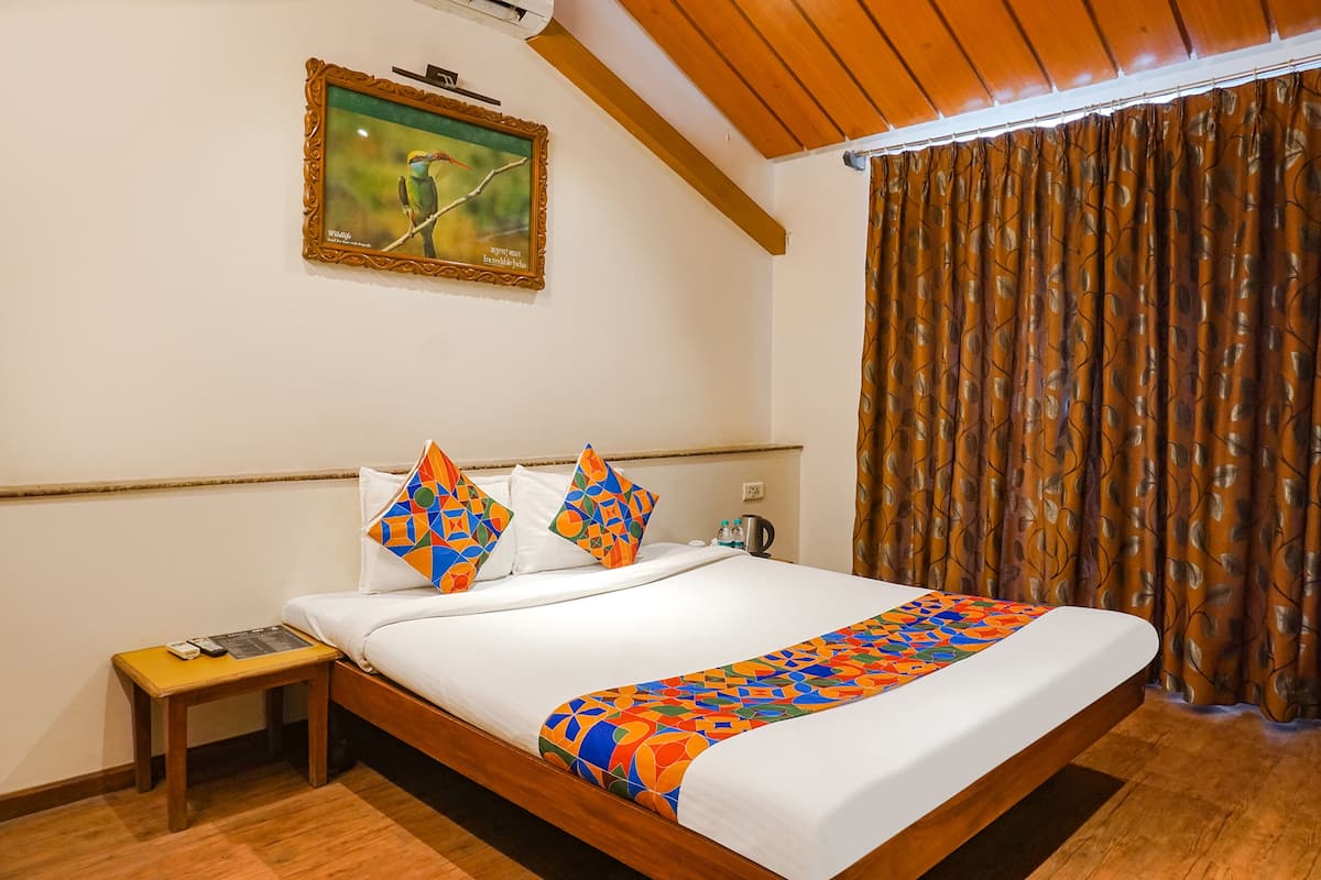 A neatly made bed with colorful pillows, a small bedside table with a remote control, and a painting on the wall.