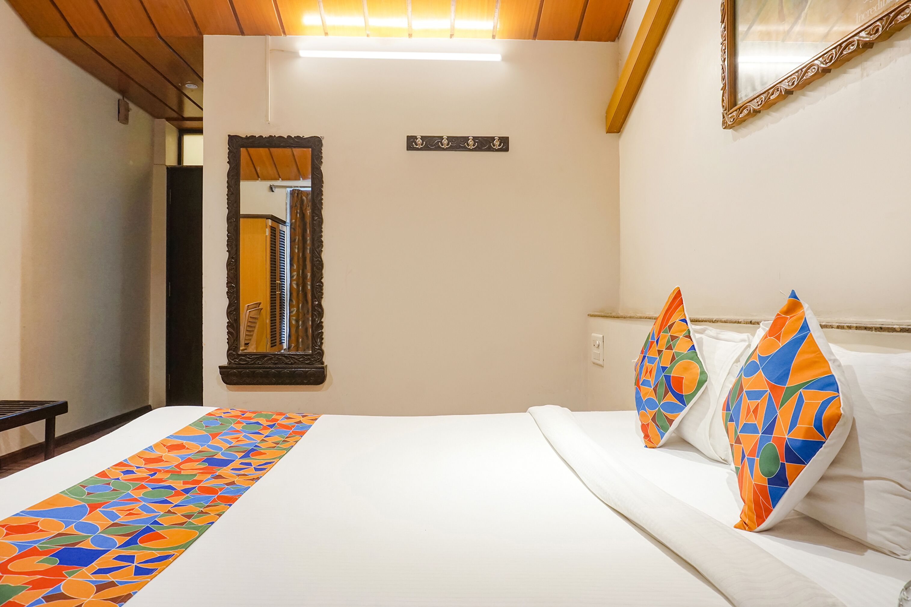 A hotel room with a bed, a long decorative runner, a mirror, and a wall-mounted light fixture.