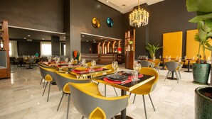 Un restaurante moderno con sillas amarillas y grises, mesas dispuestas con copas de vino y platos, y una araña.