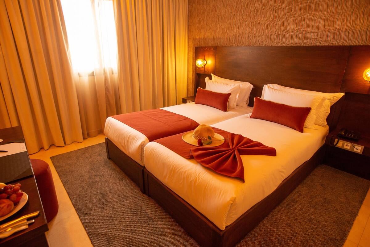 A hotel room with a large bed, two bedside tables, a nightstand, a lamp, and a fruit basket.