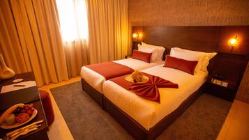 A hotel room with a large bed, two bedside tables, a nightstand, a lamp, and a fruit basket.