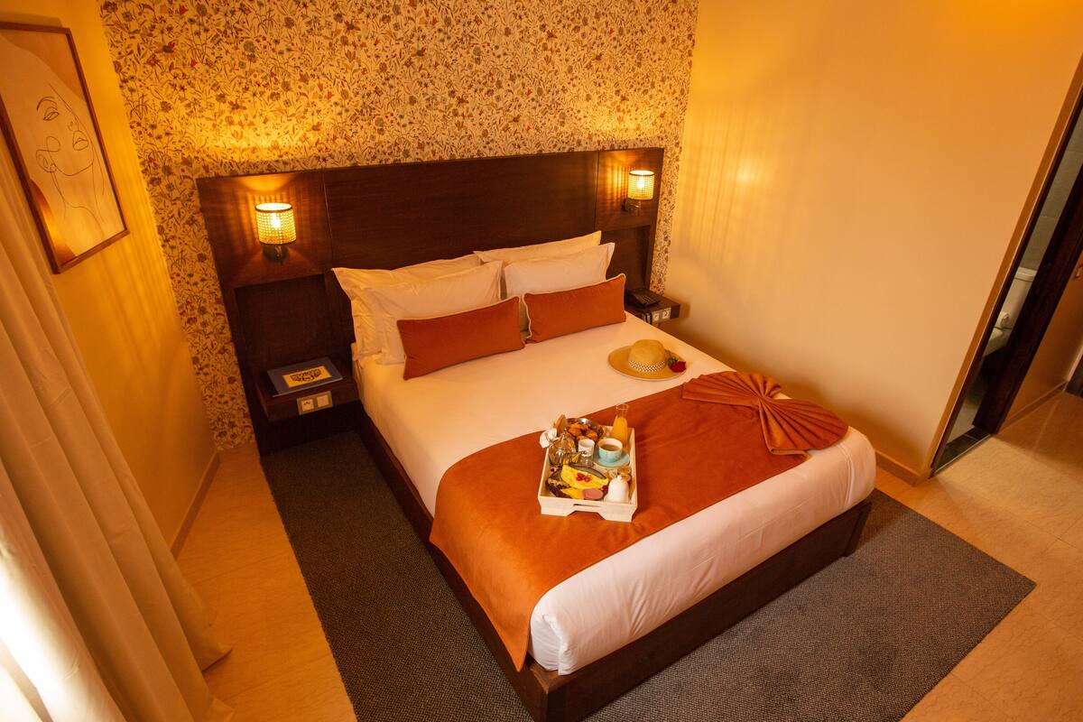 A hotel room with a large bed, a nightstand, a bedside lamp, and a tray with breakfast items.