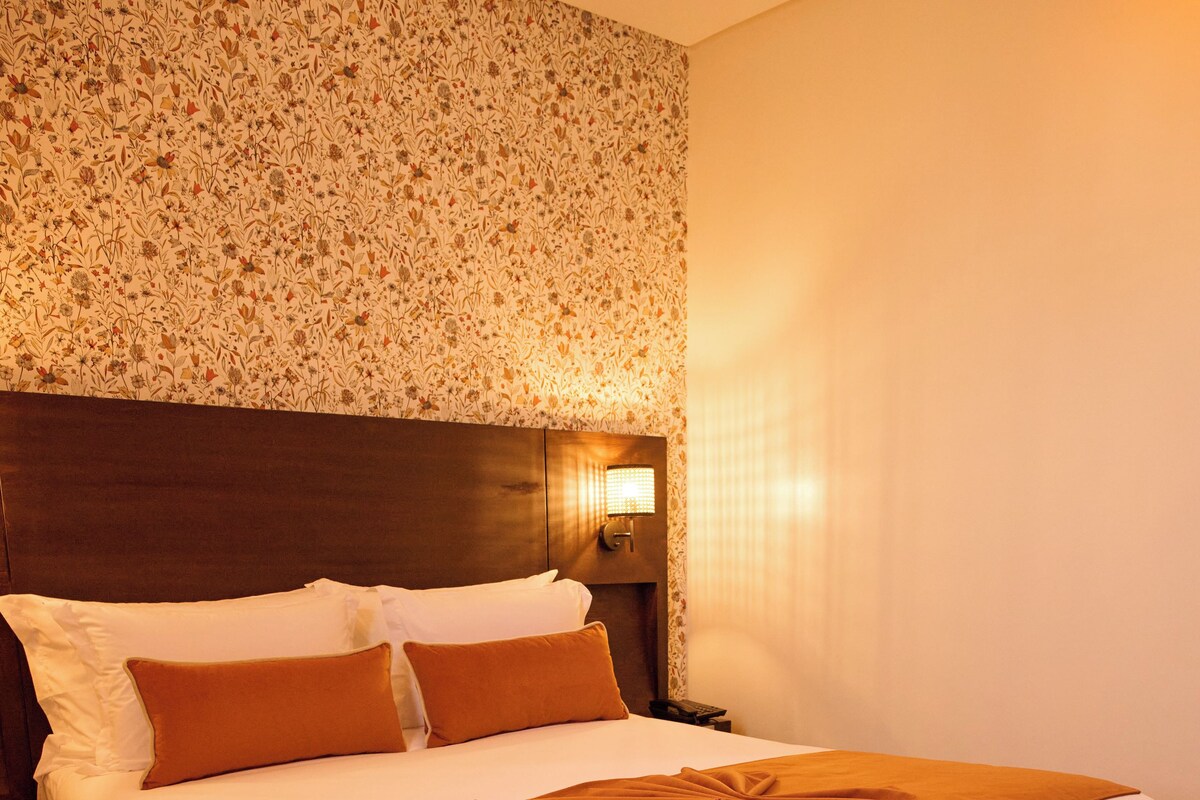 Un lit bien fait, avec une tête de lit en bois, un plaid marron et des coussins assortis.