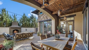 An outdoor patio with a stone fireplace, wooden furniture, and potted plants.