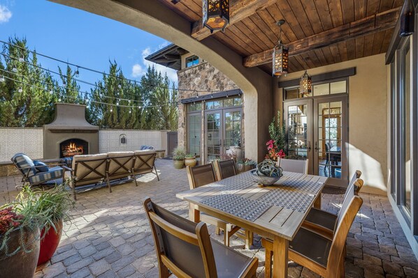 An outdoor patio with a stone fireplace, wooden furniture, and potted plants.