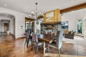 A spacious dining area with a large wooden table, stone fireplace, and a view of the kitchen. - Juniper Preserve (Pronghorn) | Golf & Mtn Views (Bend)