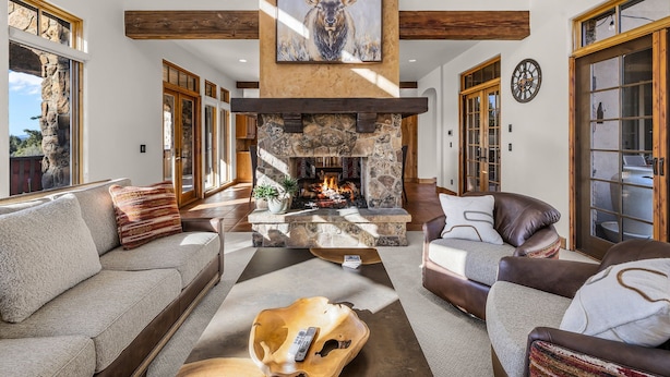 A spacious living room with a stone fireplace, leather sofas, and a large elk painting.