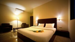 A hotel room with a large bed, bedside lamps, a desk, a chair, and an air conditioning unit. - The Aksa Hotel (Mumbai)