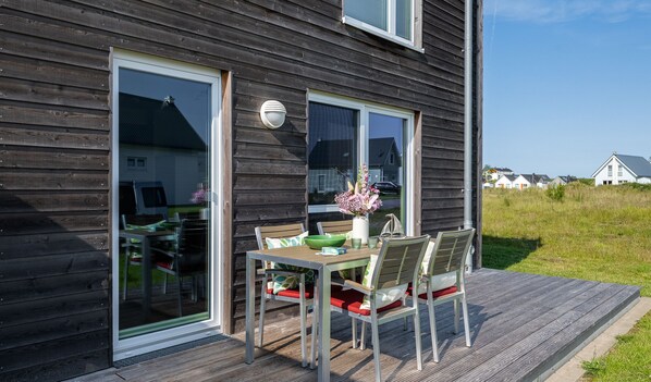 A wooden deck with a table and chairs, a vase of flowers, and a window overlooking a grassy area.