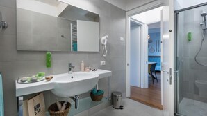 A modern bathroom with a large mirror, a sink, a shower, and a basket under the sink. - The Chic Lino Delle Fate Eco Resort Num4054 (San Michele al Tagliamento)