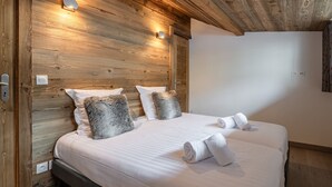 Ein Schlafzimmer mit einem hölzernen Kopfende, zwei weißen Betten und einer wandmontierten Leuchte.