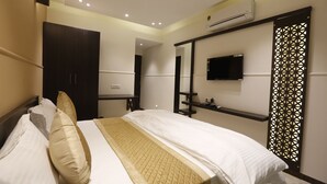 A hotel room with a bed, bedside table, TV, and an air conditioning unit. - Hotel Maple Inn (Ahmedabad)