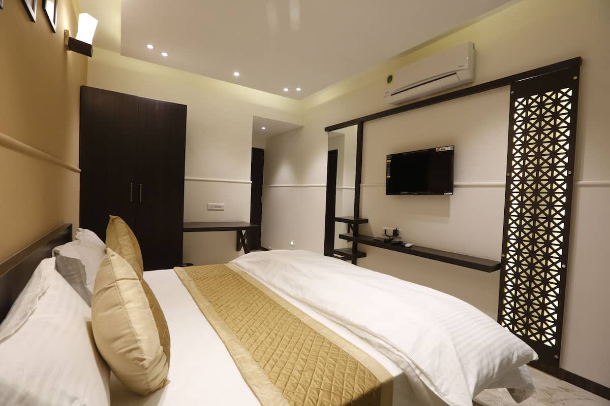 A hotel room with a bed, bedside table, TV, and an air conditioning unit.