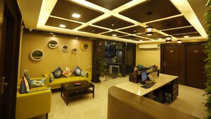 A modern hotel lobby with a reception desk, seating area, and decorative wall art. - Hotel Maple Inn (Ahmedabad)