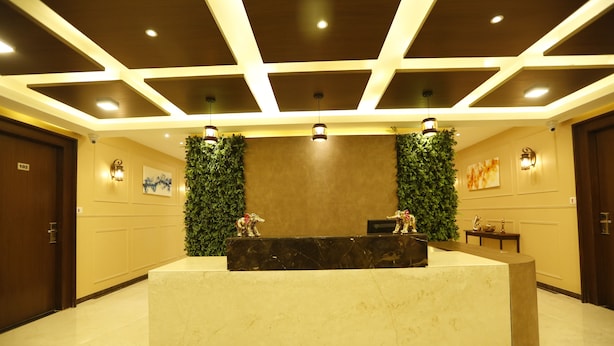A reception area with a marble counter, a green wall with plants, and a ceiling with recessed lighting. - Hotel Maple Inn (Ahmedabad)