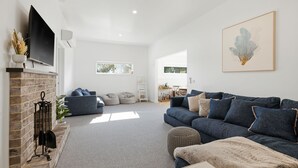 A spacious living room with a fireplace, a large sofa, and a television mounted on the wall. - The Waters Edge by Ready Set Stay (San Remo)