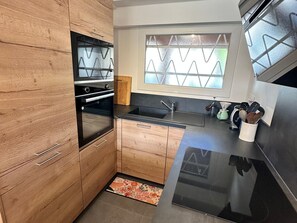 Uma cozinha moderna com armários de madeira, fogão preto, pia e janela com vidro fosco.