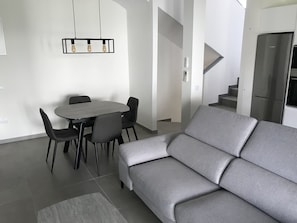 En moderne stue med en grå sofa, et rundt spisebord med stole og en minimalistisk pendellampe.